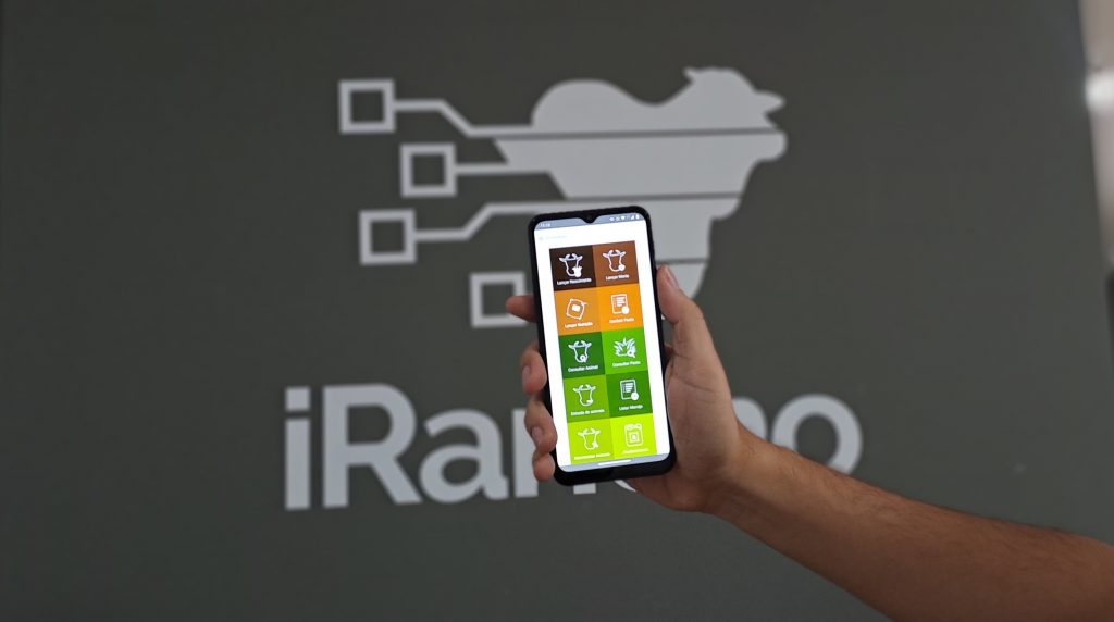 Na imagem, um mão segura um celular que está exibindo print de tela do iRancho, um software de gestão voltado para pecuária de corte.